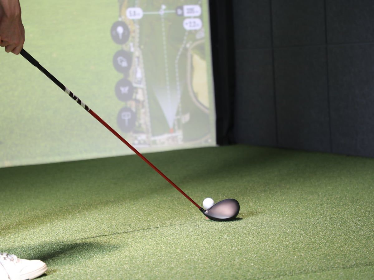 Driver und Golfball auf dem Abschlag vor der Simulatorleinwand